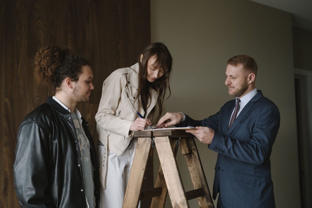 Three individuals signing a contract on a ladder inside a new house, symbolizing a real estate deal.